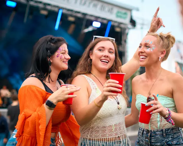 サマーミュージックフェスティバル ホールディングドリンクで楽しいグリッターを着ている3人の女性の友人 — ストック写真