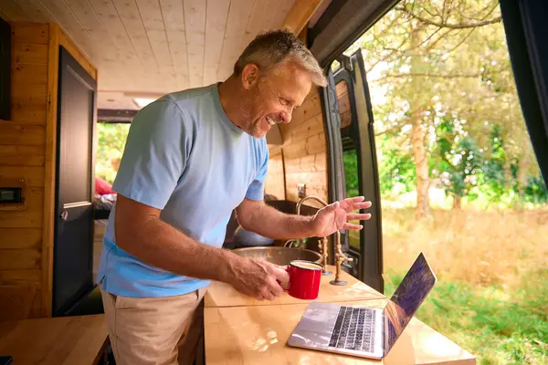 Senior Man On Camping Trip In Countryside Working Inside RV Using Laptop To Make Video Call