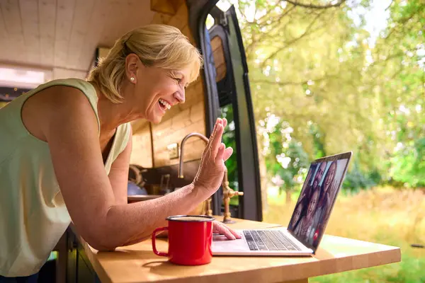 Senior Woman On Camping Trip In Countryside Working Inside RV Using Laptop To Make Video Call