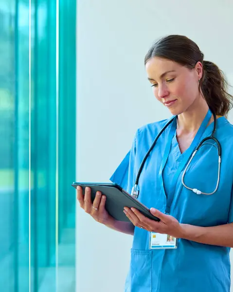 病院でデジタルタブレットを見ているスクラブを身に着けている女性医師の肖像画 — ストック写真