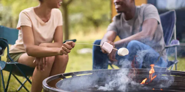 Close Up Of Couple Camping In Countryside With RV Toasting Marshmallows Outdoors On Fire