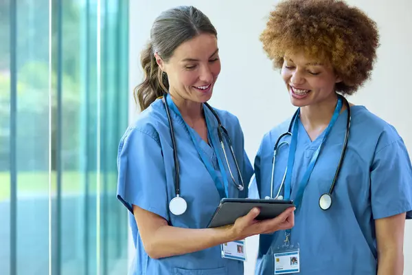 病院で患者ノートを議論デジタルタブレットでスクラブを身に着けている2人の女性医師 — ストック写真