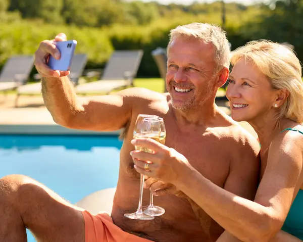 资深情侣在酒店游泳池边享用香槟酒放松度假 — 图库照片