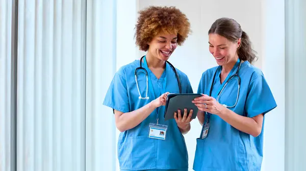 Two Female Doctors Wearing Scrubs Digital Tablet Discussing Patient Notes — Stock Photo, Image