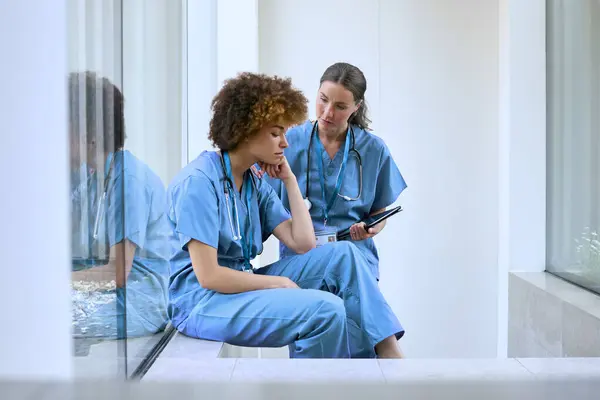 現代病院でストレスを受けた同僚を心配するスクラブを身に着けている女性医師 — ストック写真