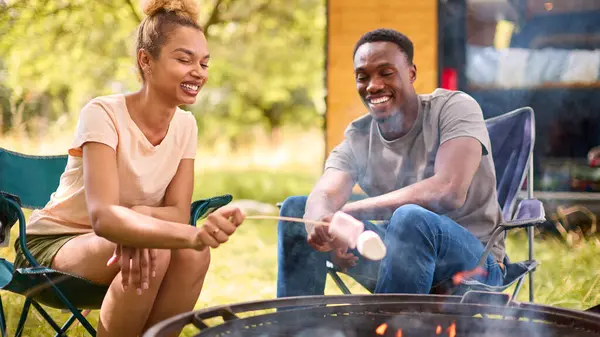 Couple Camping In Countryside With RV Toasting Marshmallows Outdoors On Fire