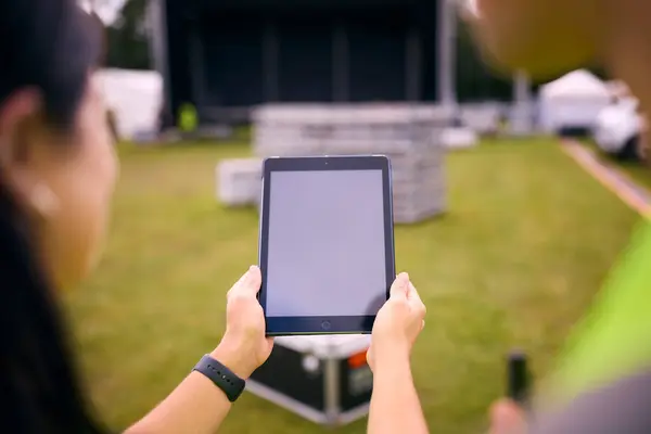 Close Up Of Production Team Looking At Digital Tablet Setting Up Outdoor Stage For Music Festival