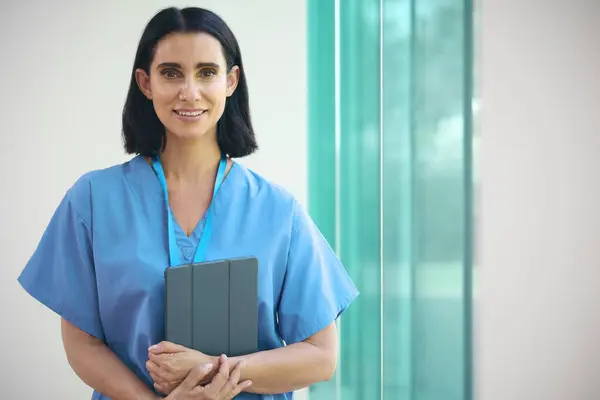 病院のデジタルタブレットが付いている成熟した笑顔の女性の医者の身に着けているスクラブの肖像画 — ストック写真