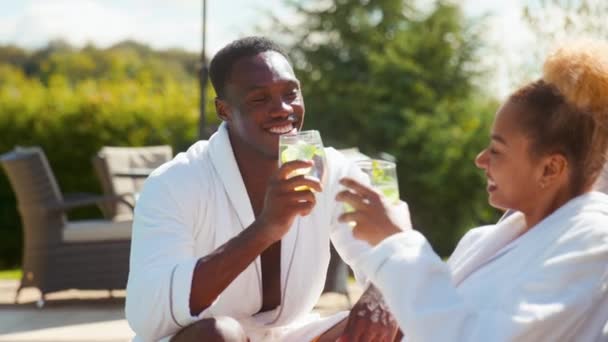 Couple Wearing Robes Outdoors Sitting Relaxing Celebrating Drinks Loungers Swimming — Stock Video