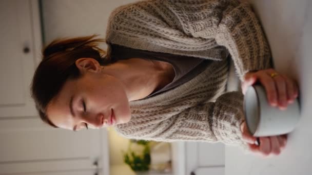一个垂直的视频 年轻女人在家里的厨房柜台上 一边喝咖啡一边休息 动作缓慢 — 图库视频影像