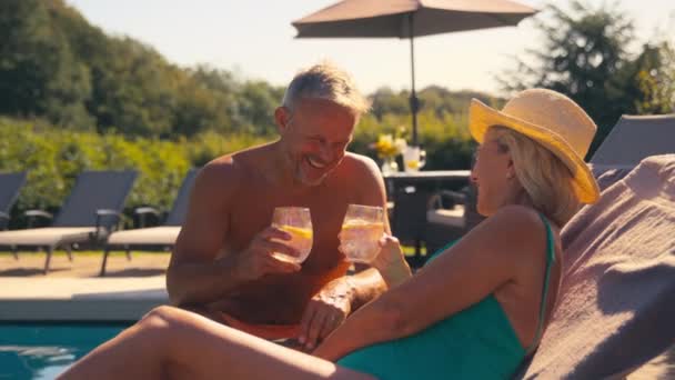 上了年纪的退休夫妇穿着游泳衣在酒店游泳池边悠闲自在地喝着不含酒精的饮料举杯庆祝暑假 动作缓慢 — 图库视频影像