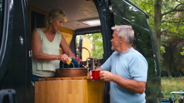 田舎でキャンプを楽しむシニアカップルは 男性がコーヒーを飲むように洗い流す女性とRvの中でリラックス — ストック動画