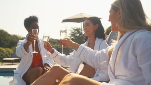 三个成熟的女性朋友穿着长袍坐在户外游泳馆边 一边喝着香槟 一边在温泉上举杯 动作缓慢 — 图库视频影像