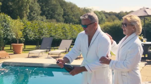 Rentnerehepaar Bademänteln Feiert Eröffnung Und Versprüht Champagner Hotelpool Auf Liegestühlen — Stockvideo
