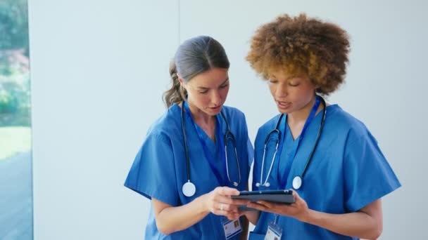 Две Женщины Доктора Скрабах Цифровыми Планшетами Обсуждают Записи Пациентов Больнице — стоковое видео