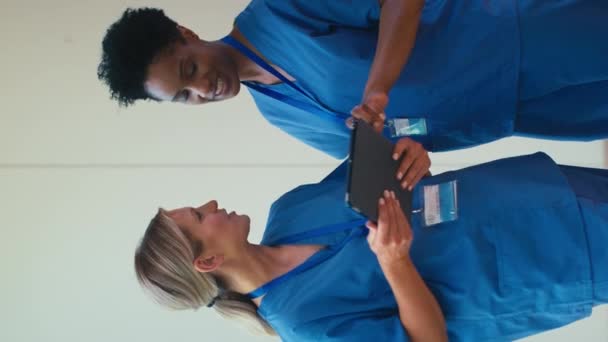 スクラブミーティングを着用し 病院でデジタルタブレットをチェックする2人の笑顔の成熟した女性医師の垂直ビデオ スローモーションで撮影 — ストック動画