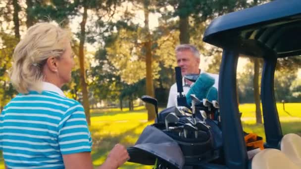 上級引退したカップルは クラブを選択する前にコース上のゴルフバギーから抜け出す スローモーションで撮影 — ストック動画