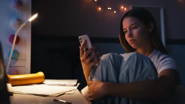 忧心忡忡的少女晚上坐在卧室的办公桌前 用手机发短信 动作缓慢 — 图库视频影像