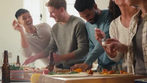 Grupa Przyjaciół Domu Kuchni Dodawanie Toppings Domowej Pizzy Imprezę Razem — Wideo stockowe