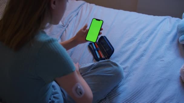 自宅でベッドに座っている糖尿病の女の子のクローズアップ携帯電話アプリでインスリンレベルをチェック — ストック動画