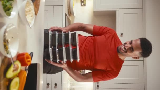 キッチンで笑顔の男の垂直ビデオ肖像画 フィットネス服を着て冷蔵庫のために事前に健康的な食事のバッチを作る スローモーションで撮影 — ストック動画