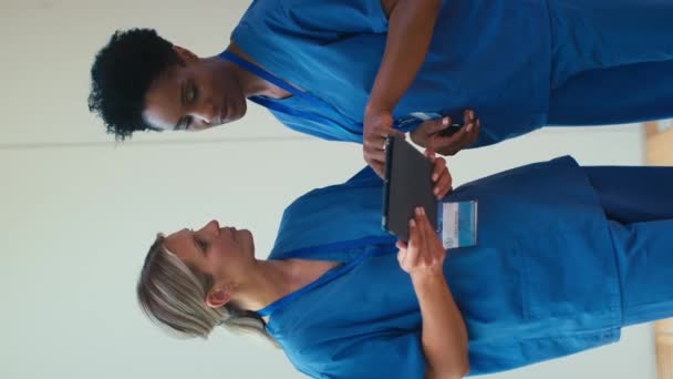 スクラブミーティングを着用し 病院でデジタルタブレットをチェックする2人の笑顔の成熟した女性医師の垂直ビデオ スローモーションで撮影 — ストック動画