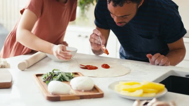 ダウン症の男性と一緒に自宅で夫婦の近くにトマトソースを一緒にキッチンで食事のための自家製ピザベースに置く女性 スローモーションで撮影 — ストック動画