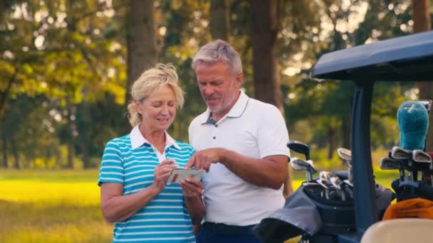 上了年纪的退休夫妇站在高尔夫球车旁边 标志着成绩卡 慢动作射门 — 图库视频影像
