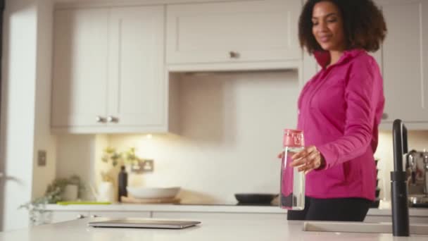 身穿健美服装 提着水瓶的女人走进厨房 在笔记本电脑上工作 动作缓慢 — 图库视频影像