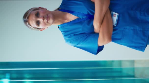 病院の折りたたみ腕のスクラブを身に着けている深刻な成熟した女性医師の垂直ビデオ肖像画 スローモーションで撮影 — ストック動画