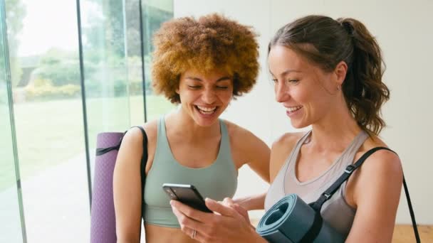 两名女性朋友穿着运动服或瑜伽工作室的运动服 看着并笑着看手机 动作缓慢 — 图库视频影像