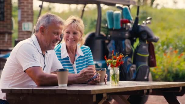 スコアカードを一緒に見てゴルフのラウンド後にコーヒーを持っているシニア引退したカップル スローモーションで撮影 — ストック動画