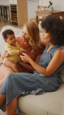 Two women are seated comfortably on a couch, engaging with an adorable baby. The atmosphere is warm and inviting, filled with laughter and joy as they share a special moment together.   clipart