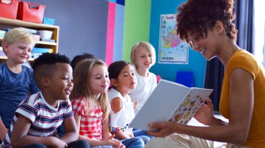 Group Of Elementary School Pupils Sitting On Floor Listening To Female Teacher Read Story clipart