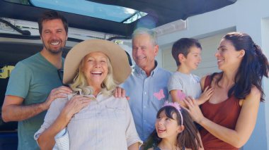 Portrait Of Multi Generation Family Loading Luggage Into Back Of Car Leaving For Summer Vacation clipart