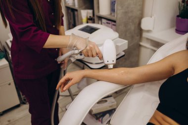 Güzel bir kız lazer radyasyonundan dolayı kırmızı gözlüklü bir güzellik uzmanının ofisinde yatıyor. Doktorun elleri eline lazer cihazıyla saç kesiyor.