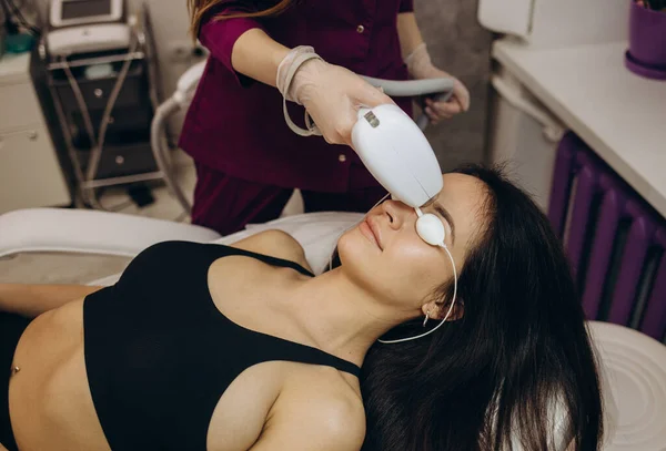 Therapist beautician makes a laser treatment to young woman\'s face at beauty SPA clinic. Facial laser hair removal epilation procedures. Close up, selective focus.