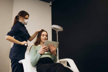 Doktor, özel dermatoloji ekipman sistemi, saç dökülmesi ve trikoloji konsepti olan genç bir kızın kafa derisini inceliyor..