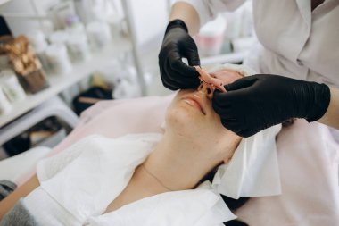 Güzellik uzmanı, kaplıca salonundaki genç bir kadının yüzünden kilden bir maske çıkarıyor. Güzellik uzmanındaki güzel genç kız spa prosedürlerini yapıyor.