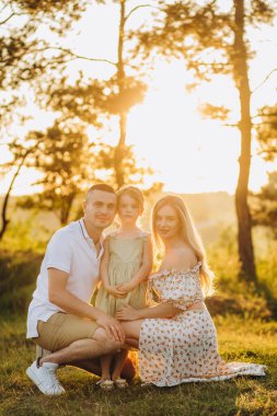 Mutlu Aile parkı akşam ışık. Bir güneş ışıkları. Anne, baba ve bebek mutlu gün batımında yürümek. Mutlu bir aile kavramı. Ebeveynler bebeğin ellerini tutun.