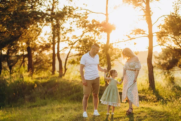 Happy family in the park evening light. The lights of a sun. Mom, dad and baby happy walk at sunset. The concept of a happy family.Parents hold the baby\'s hands.