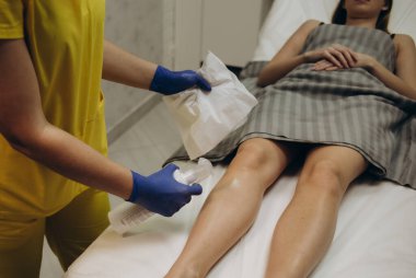 Cosmetologist is sprinkling and distributing talcum powder on a young girl's leg before the epilation procedure. The girl is lying on a couch in a beauty salon, she does the procedure shugaring