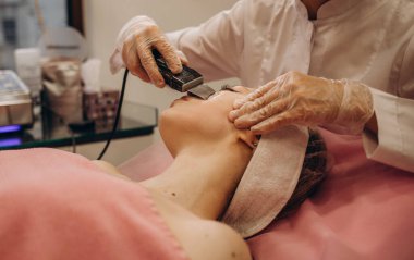 Genç ve güzel bir kadın güzellik salonlarında tedavi görüyor. Ofisteki güzel, koyu saçlı kadın kanepede uzanıyordu. Ultrasonik temizlik prosedürü. Donanım kozmetolojisi.