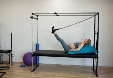 Pregnant woman exercising with the help of reformer on pilates class
