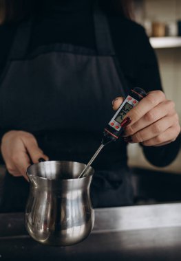 Homemade candle making session using soy wax and assorted glass containers. Photo shows a pair of hands using a thermometer to check the temperature of soy wax.