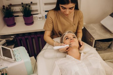 Close-up portrait of a beautiful woman with closed eyes and apparatus for skin rejuvenation. Beauty salon procedures. RF lifting. Microcurrents.