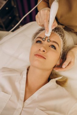 Close-up portrait of a beautiful woman with closed eyes and apparatus for skin rejuvenation. Beauty salon procedures. RF lifting. Microcurrents.