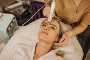 Close-up portrait of a beautiful woman with closed eyes and apparatus for skin rejuvenation. Beauty salon procedures. RF lifting. Microcurrents.