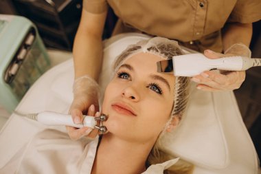 Close-up portrait of a beautiful woman with closed eyes and apparatus for skin rejuvenation. Beauty salon procedures. RF lifting. Microcurrents.
