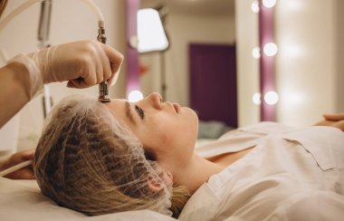 Kozmetik uzmanı, güzellik salonundaki güzel, genç bir kadının yüz derisinin mikro cilt bakımını yapıyor. Kozmetoloji ve profesyonel cilt bakımı..